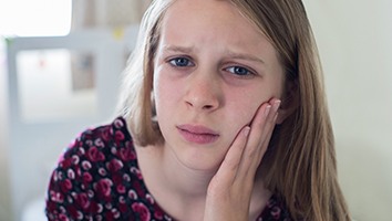 Preteen girl with braces holding cheek
