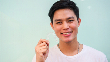 Teen boy in white shirt holding Invisalign clear aligner in Webster