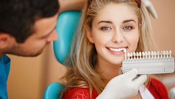 Dentist holding shade guide close to patient’s teeth