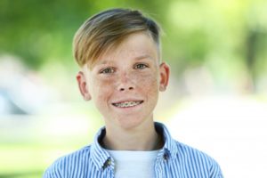 Boy in collared shirt with braces smiling after orthodontic treatment coverage