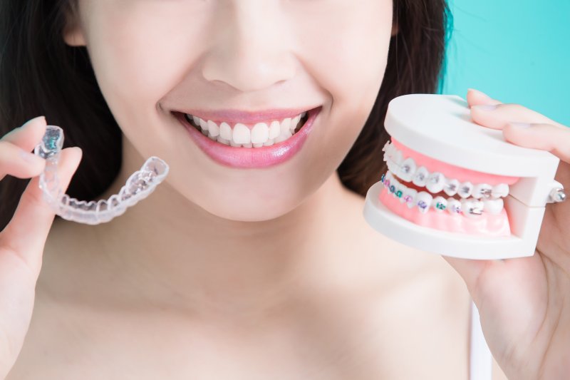 Smiling woman holding braces and Invisalign