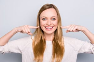 Woman who got teeth whitening after braces pointing to her smile