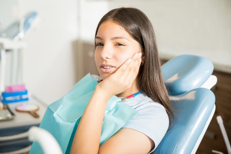 Patient with broken braces holding her cheek in orthodontic office